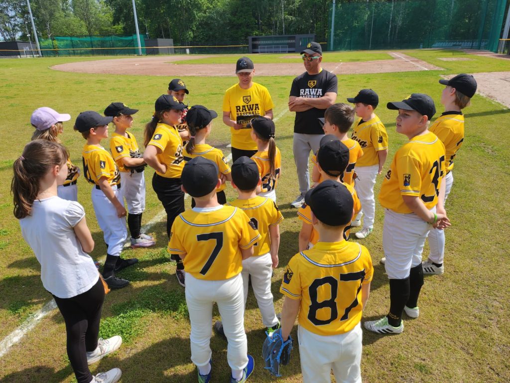 Grupa młodych baseballistów stoi wokół trenera. Boisko w Katowicach, trener mówi do zawodników ustalenia.